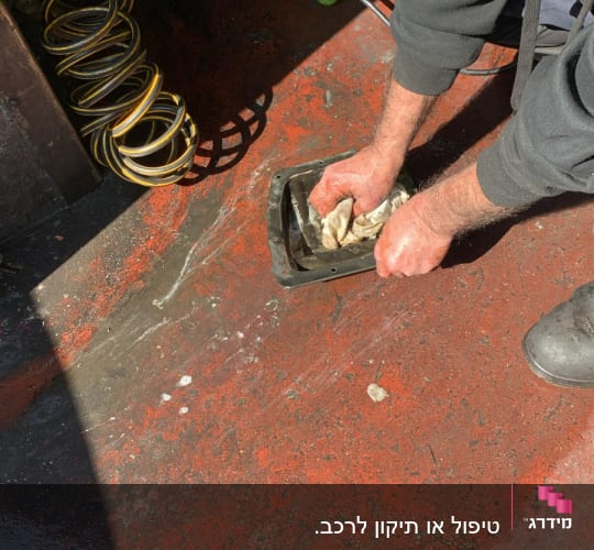 אדם מנקה חלק מתכת עם מטלית על רצפה אדומה